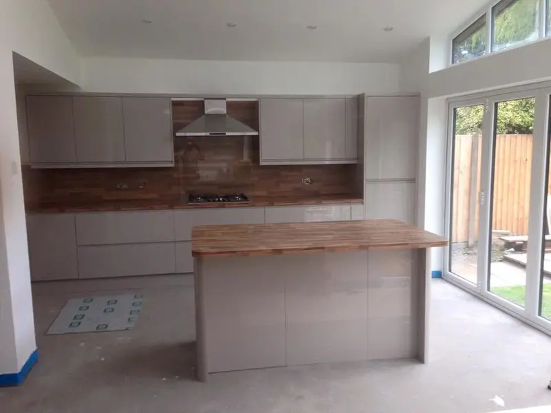 Cashmere gloss handleless kitchen with oak-effect worktops, matching wall panels and an island, with conservatory doors to the garden