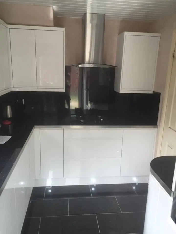 White gloss handleless kitchen with black sparkle worktops and splashback, plinth lights and dark floor tiles