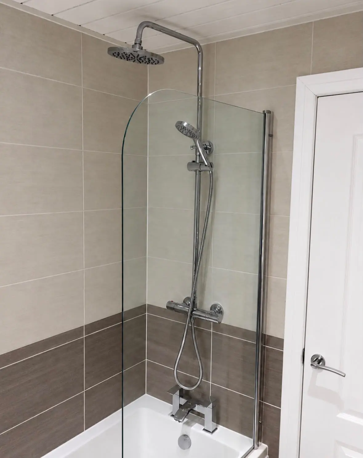 Bath with a curved glass screen and thermostatic rain shower, light tiles above a dark grey band