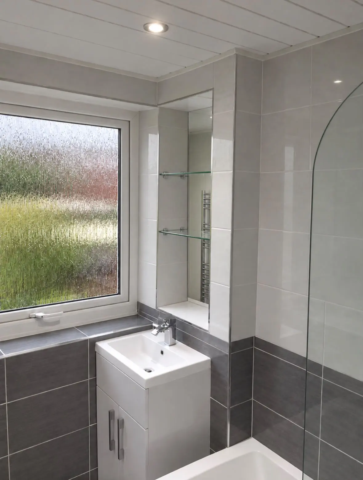 Basin unit beneath the window, beside a recessed alcove with glass shelves