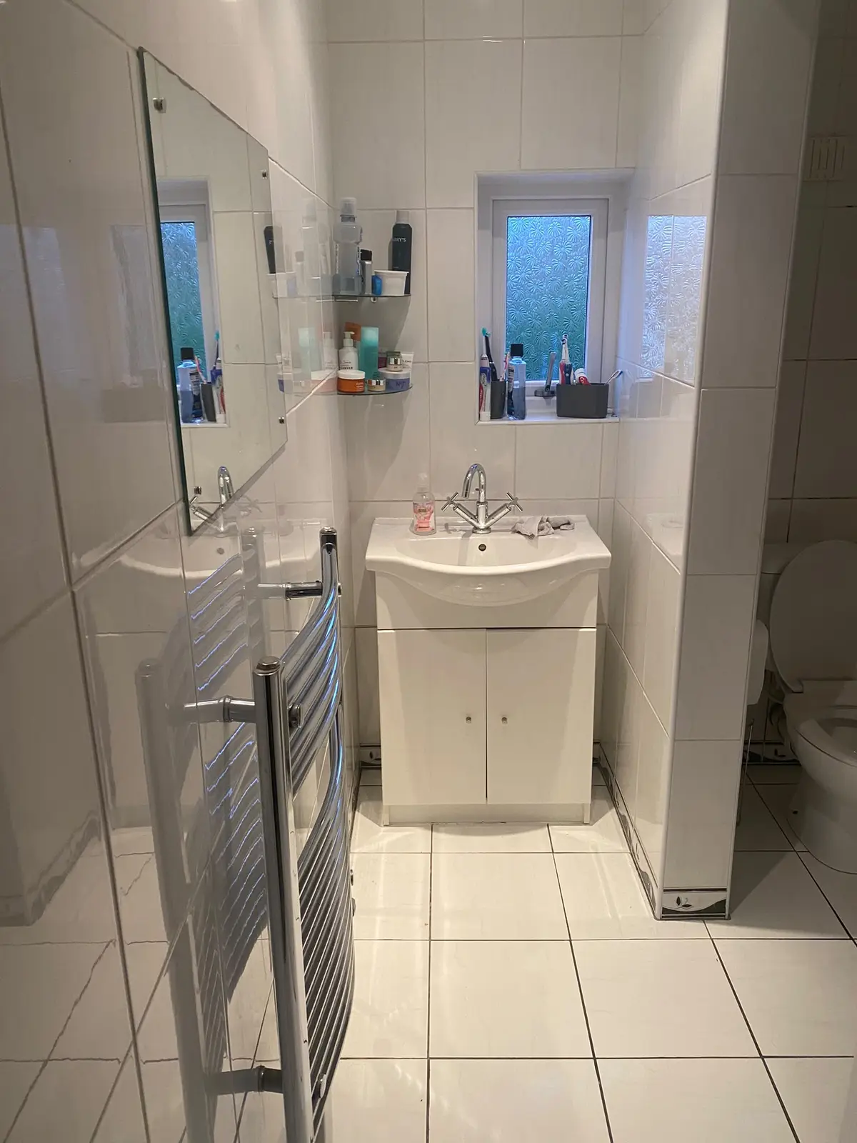 The original bathroom, with white tiles, a basin and a chrome towel radiator