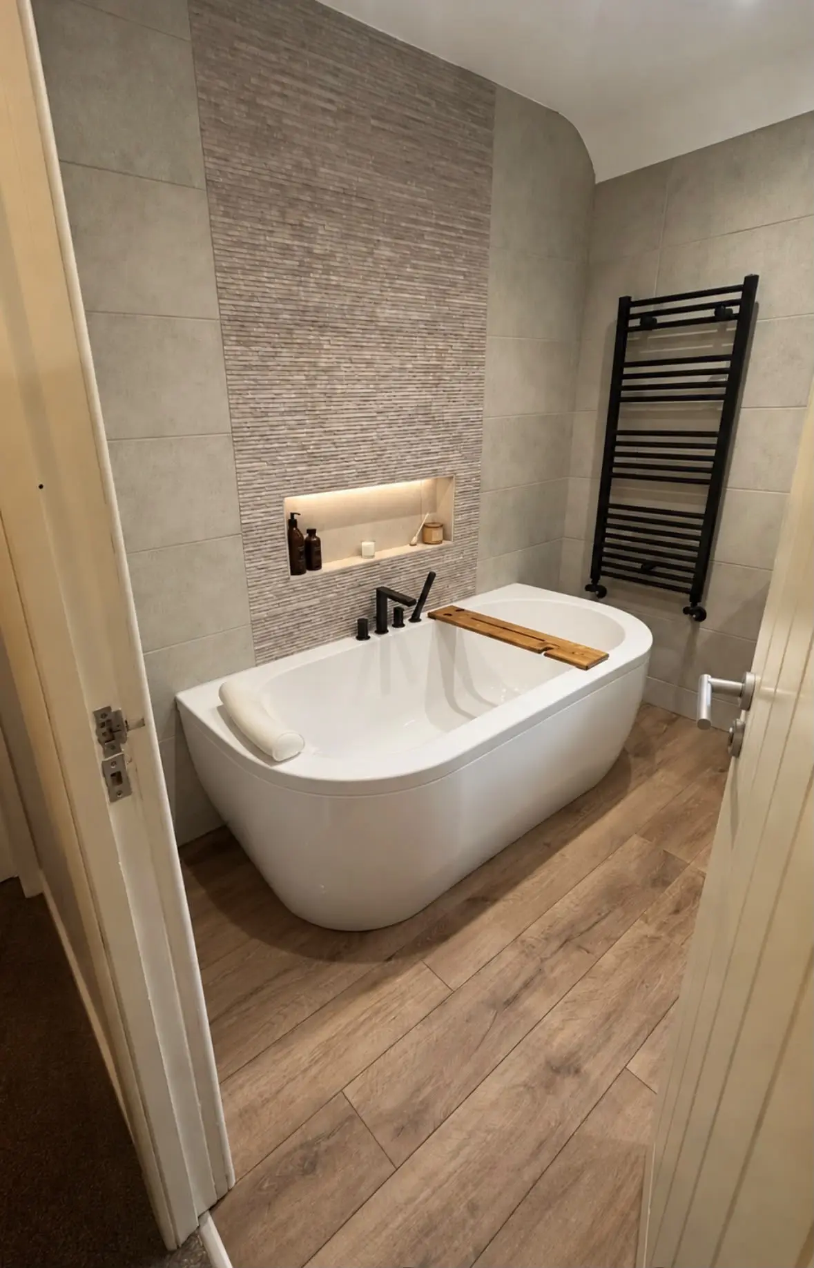 Freestanding bath beneath a lit alcove, with a black towel radiator