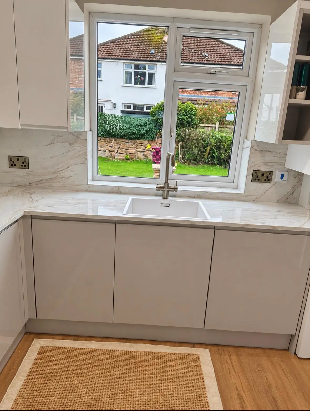 Grey gloss handleless sink run beneath the window, with a marble-effect worktop and splashback