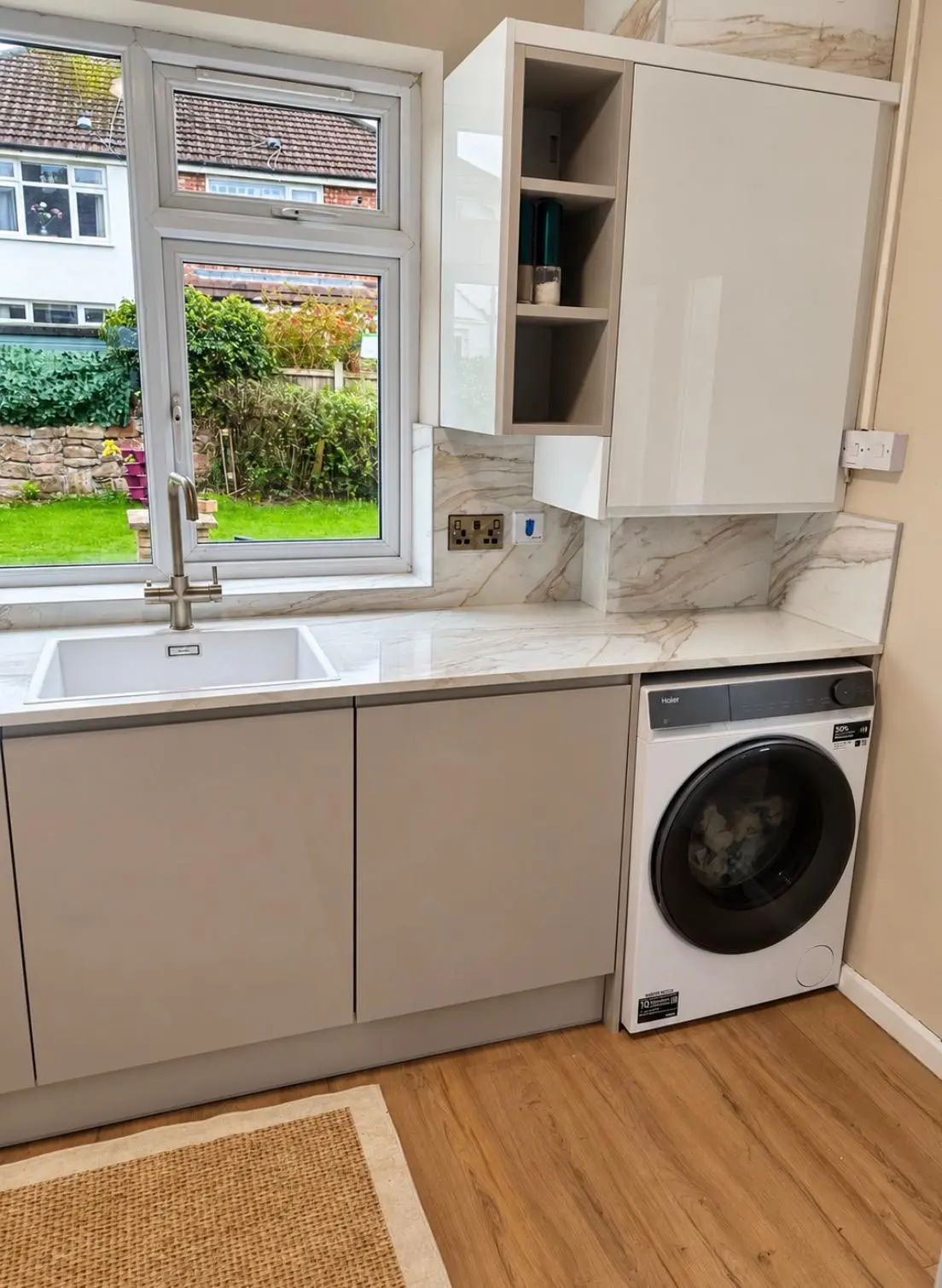 Washing machine under the worktop beside open shelving and a white gloss wall unit