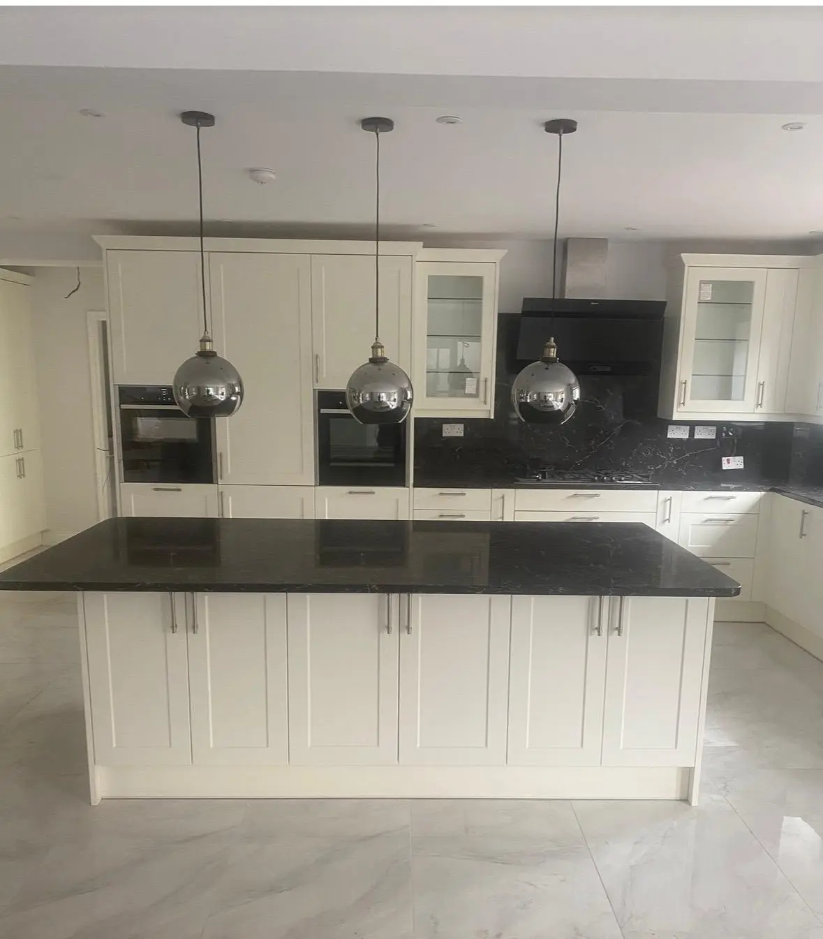 Cream shaker kitchen with a large island, black marble worktops and three pendant lights