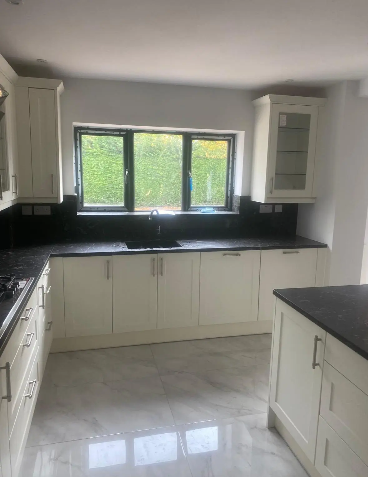 Cream shaker sink run beneath the window, with black marble worktops