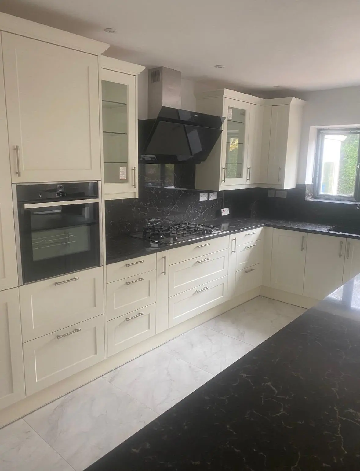 Cream shaker kitchen with a built-in oven, glazed wall cabinets and black marble splashback