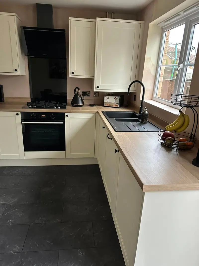Cream shaker U-shaped kitchen with wood-effect worktop, black sink and tap, black built-in oven and dark LVT floor