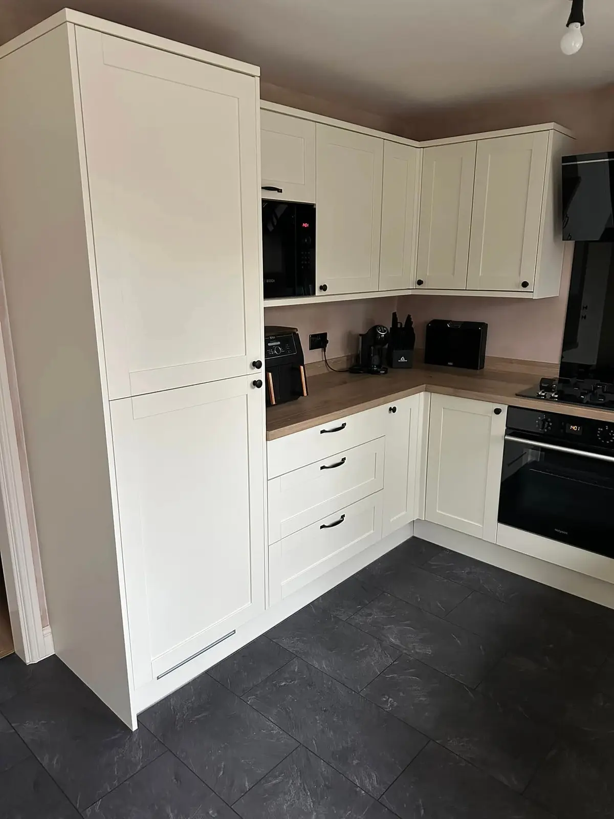 Tall cream shaker housing and wall units with black appliances and wood-effect worktop