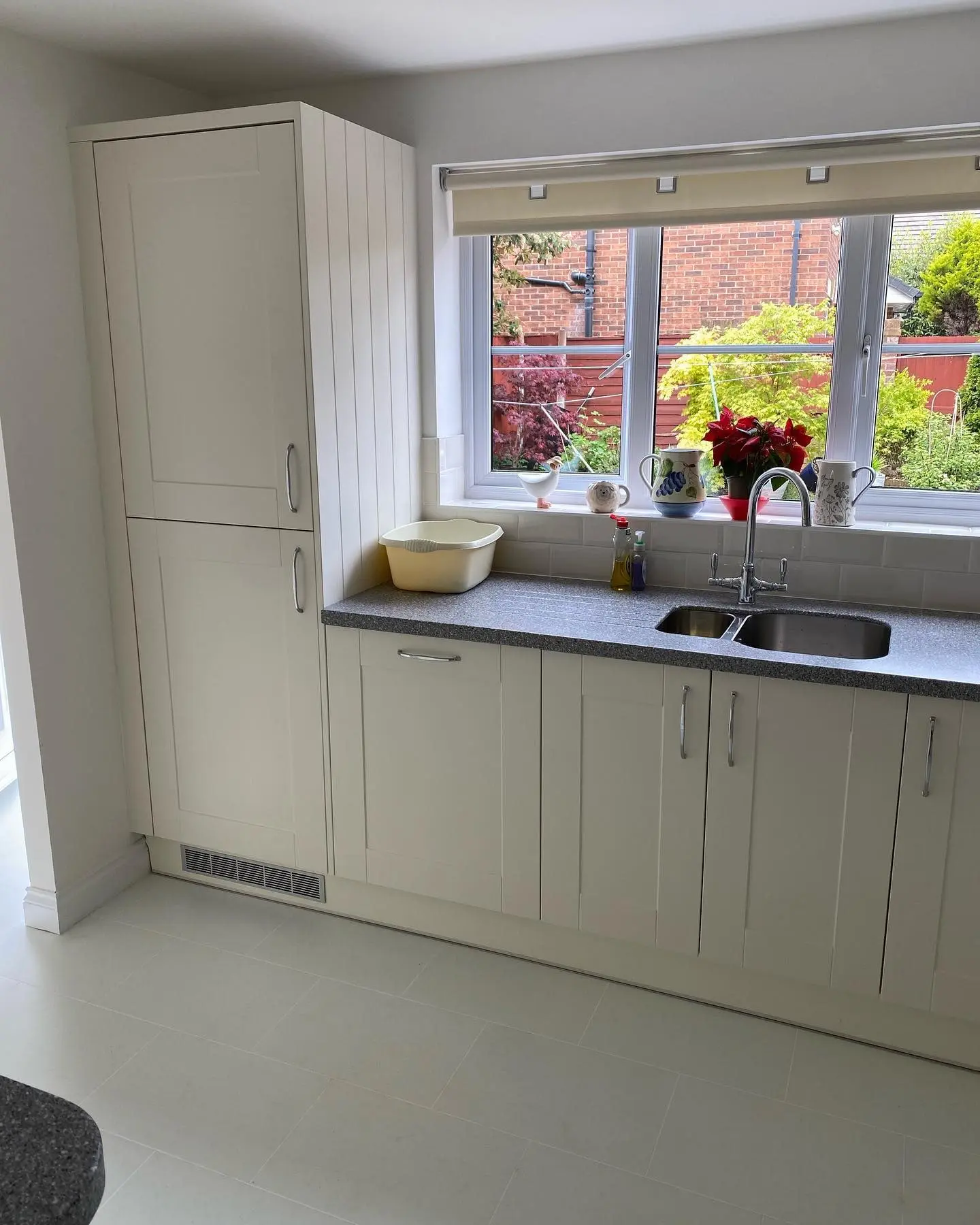 Cream shaker L-shaped kitchen with grey quartz worktops, white metro tiling and a window onto the garden