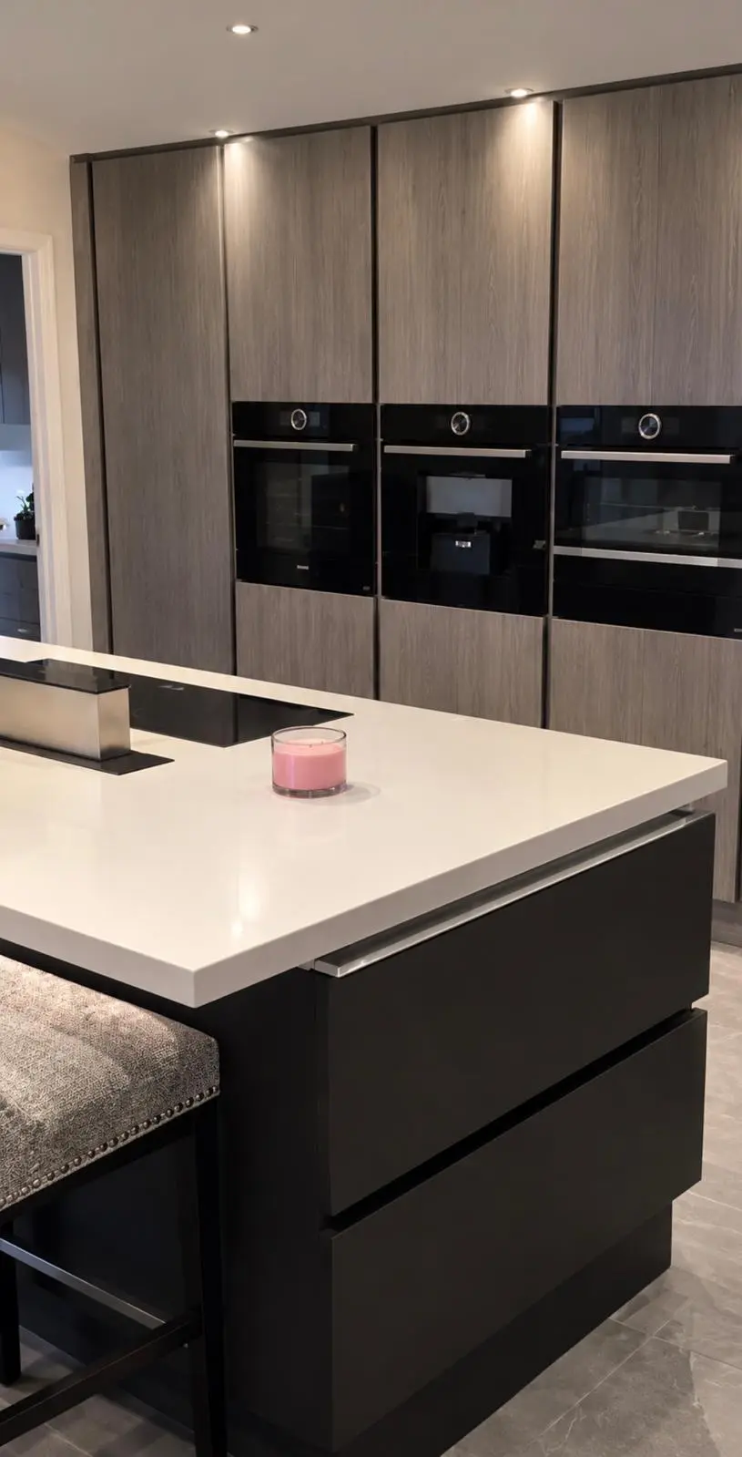 Dark handleless island with seating, in front of wood-effect high-gloss tall units with three built-in ovens