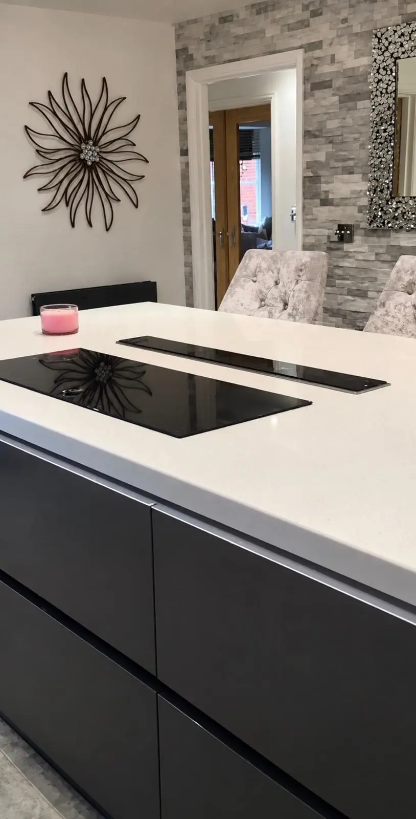 Dark gloss handleless island with a white worktop and induction hob, a stone-clad feature wall behind