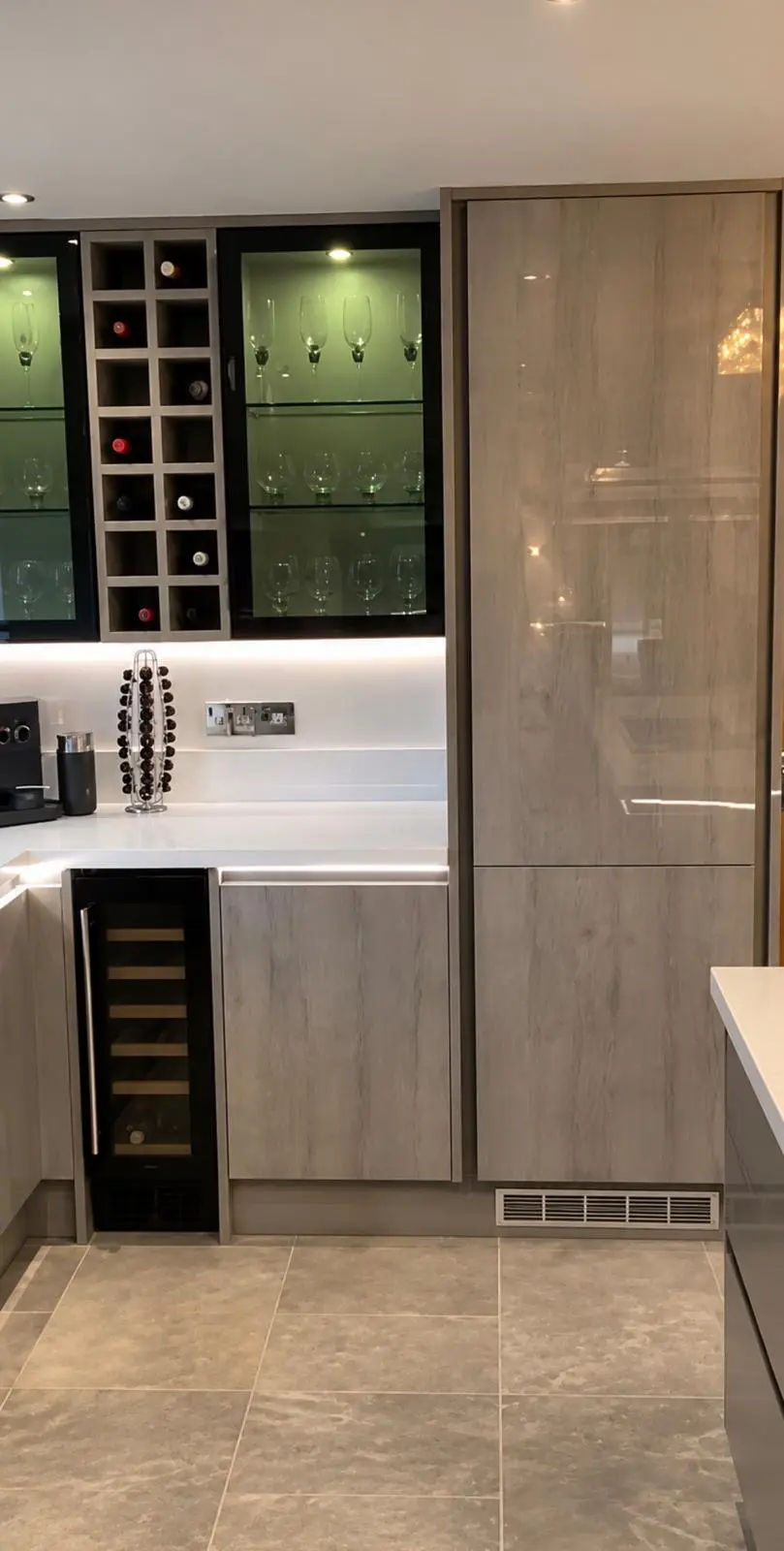 Wood-effect high-gloss tall housings beside a wine rack, glazed wall cabinets and an under-counter wine cooler
