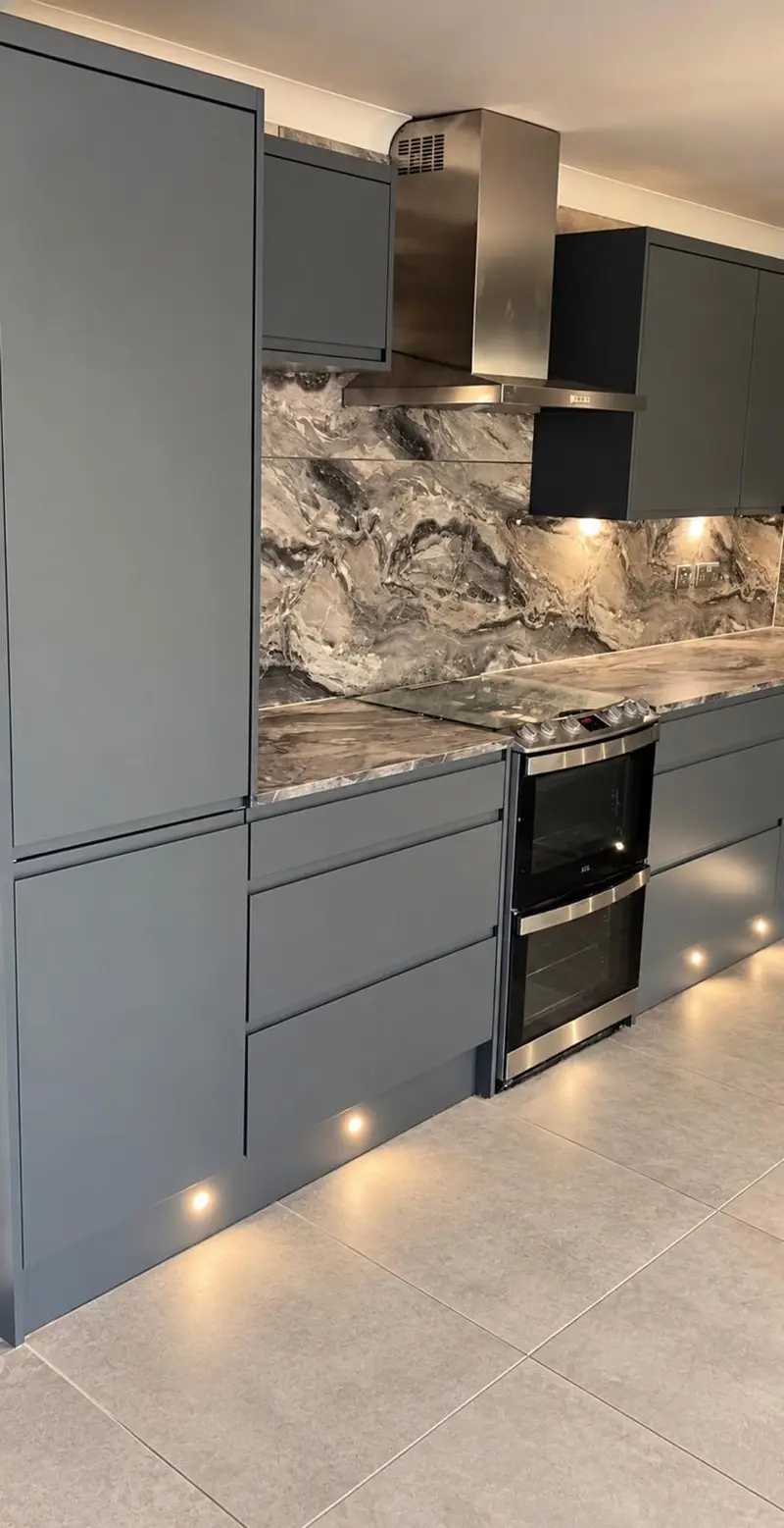 Lava grey handleless kitchen with a tall housing, double oven and chimney extractor, and plinth lights along the floor