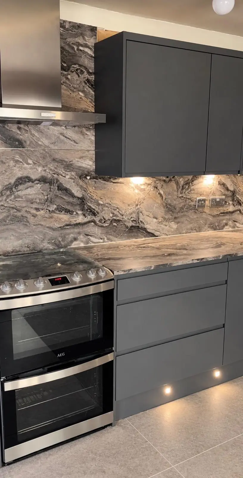 Stainless chimney extractor and double oven beside lava grey drawers and a marble-effect worktop