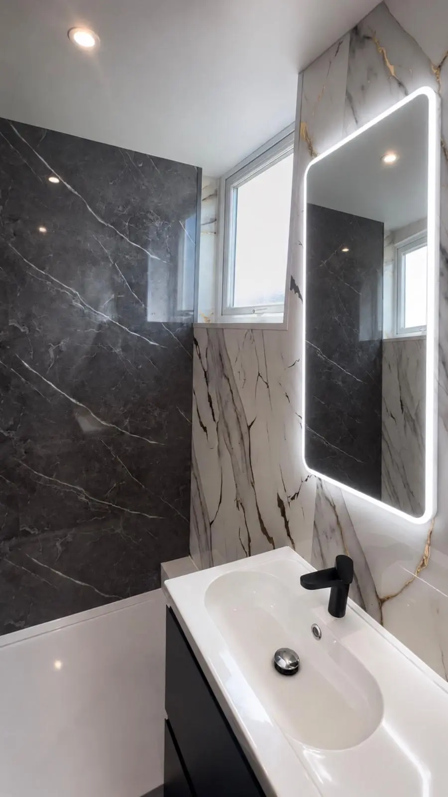 Illuminated mirror above a white basin on a black vanity unit