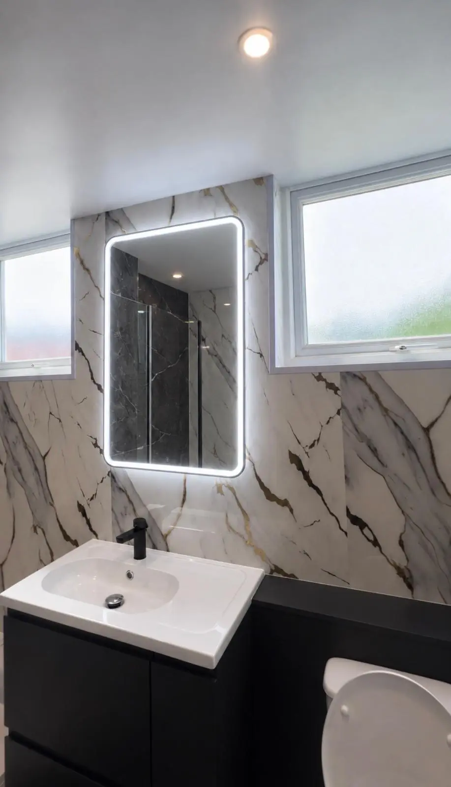 Black vanity unit, illuminated mirror and WC beneath the window