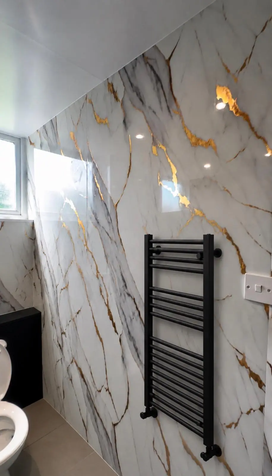 Black towel radiator on a gold-veined marble-effect wall