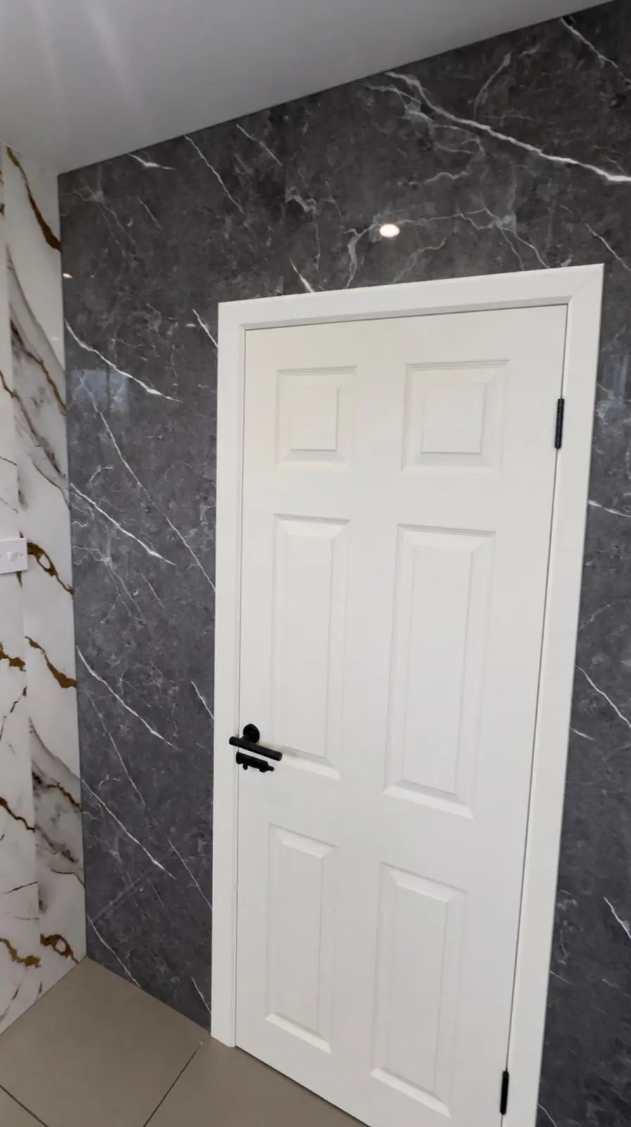 White panelled door with a black handle, set in dark marble-effect panels