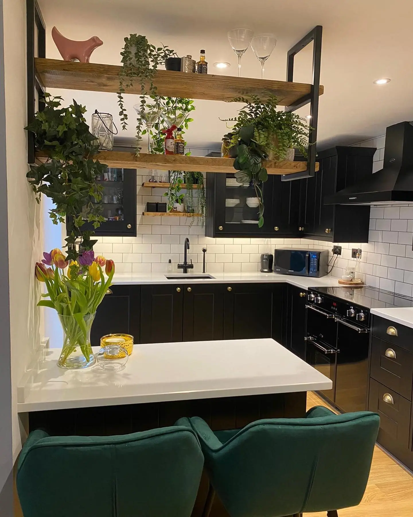 Matt black shaker kitchen with white quartz worktops, white metro tiles and suspended timber shelving with plants