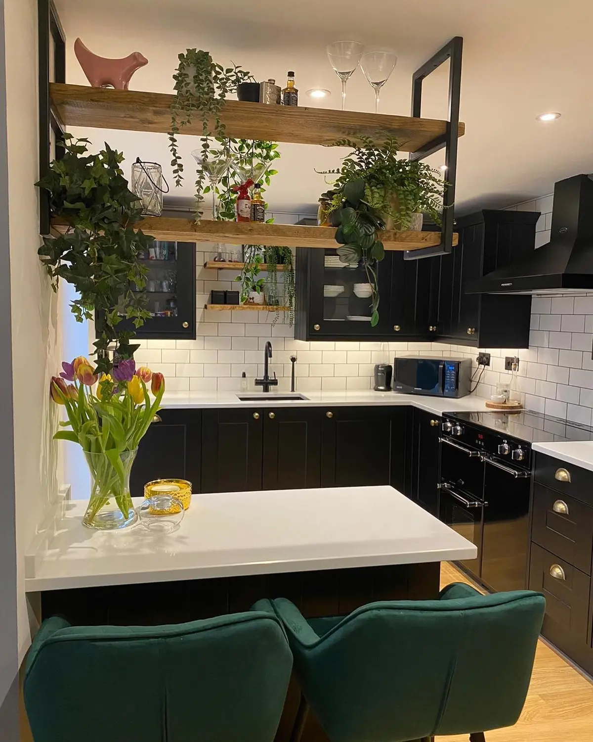 Matt black shaker kitchen with white quartz worktops, white metro tiles and suspended timber shelving with plants