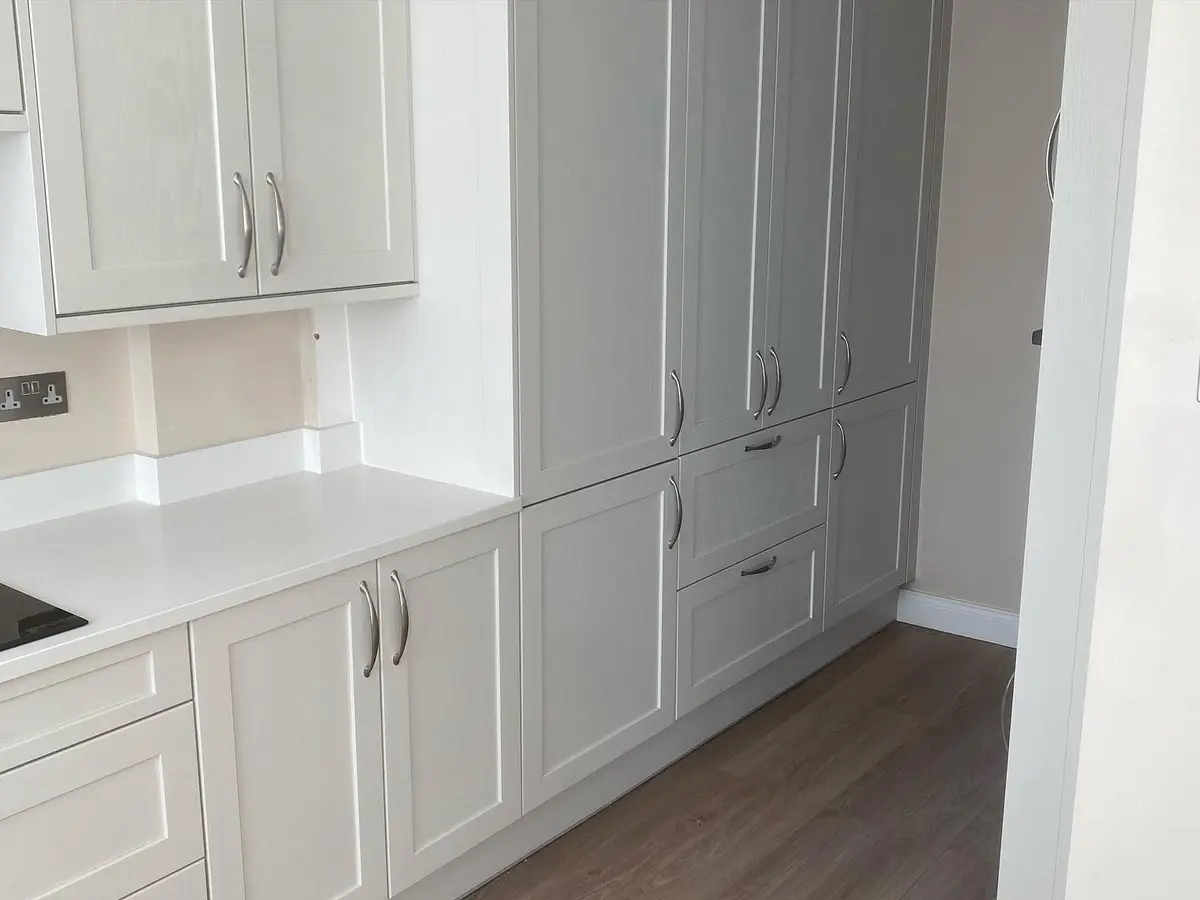 Light shaker tall larder units beside a run with quartz worktop and upstands