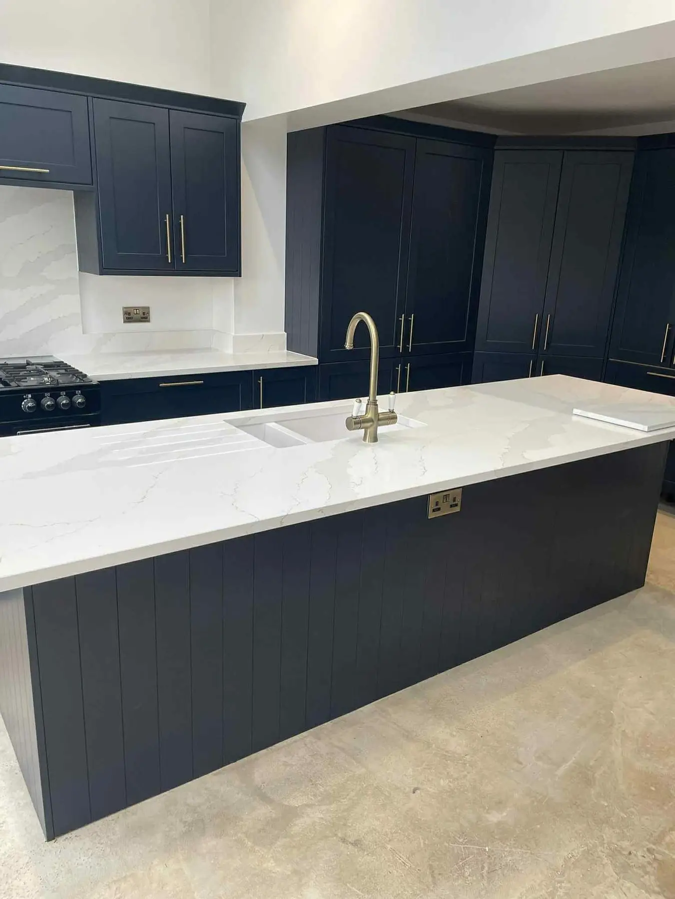 Navy shaker kitchen with a long island, white quartz worktop and brass tap, in a new extension