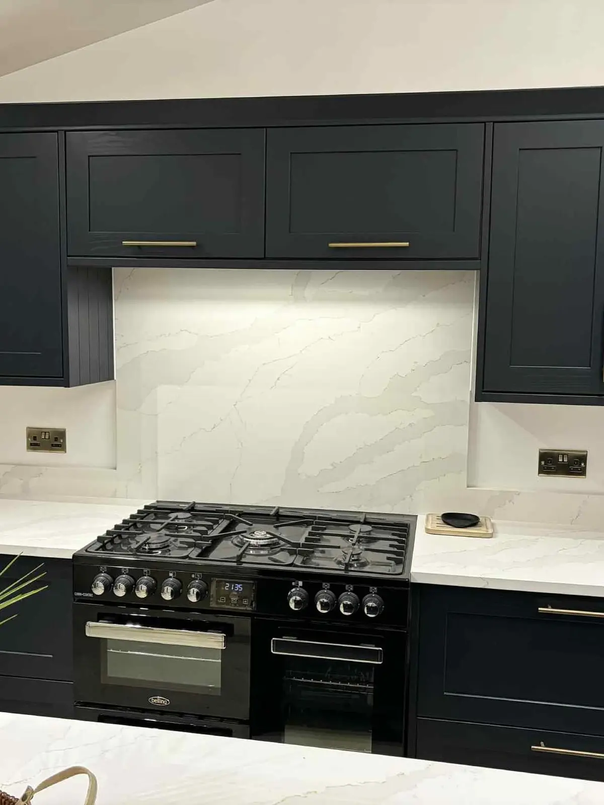 Full-height quartz splashback behind a black range cooker, framed by navy shaker units