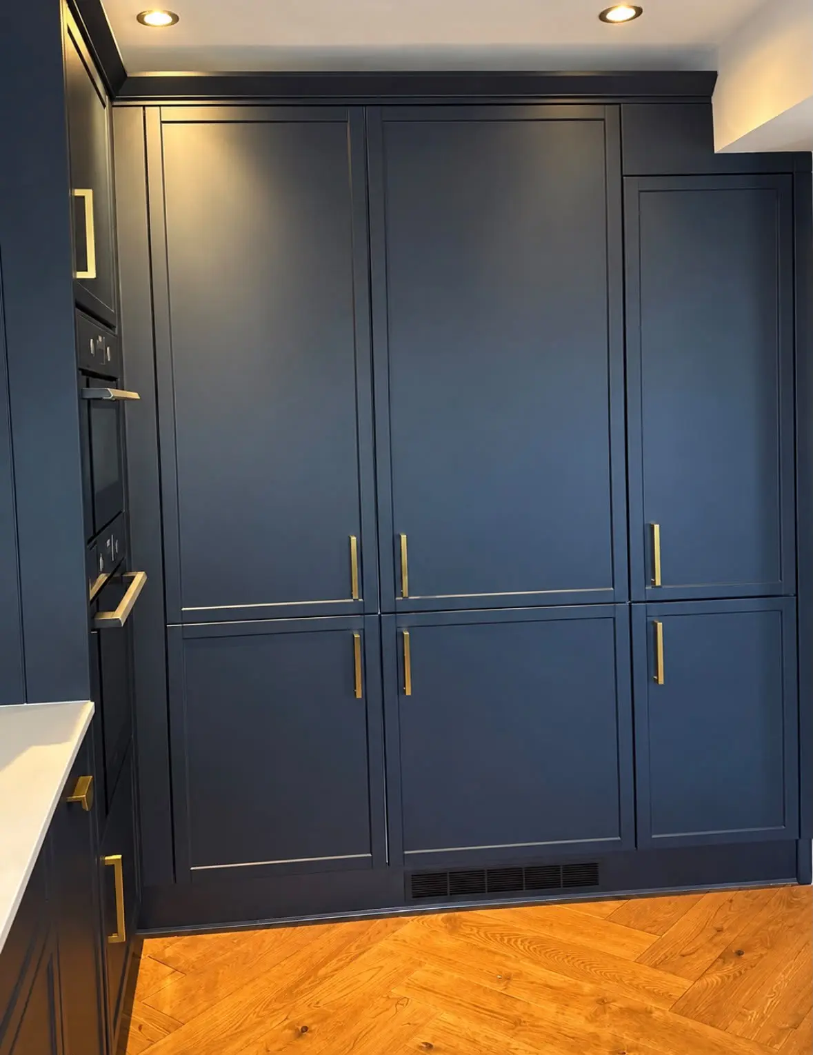 Navy shaker tall larder units with gold handles on a herringbone floor