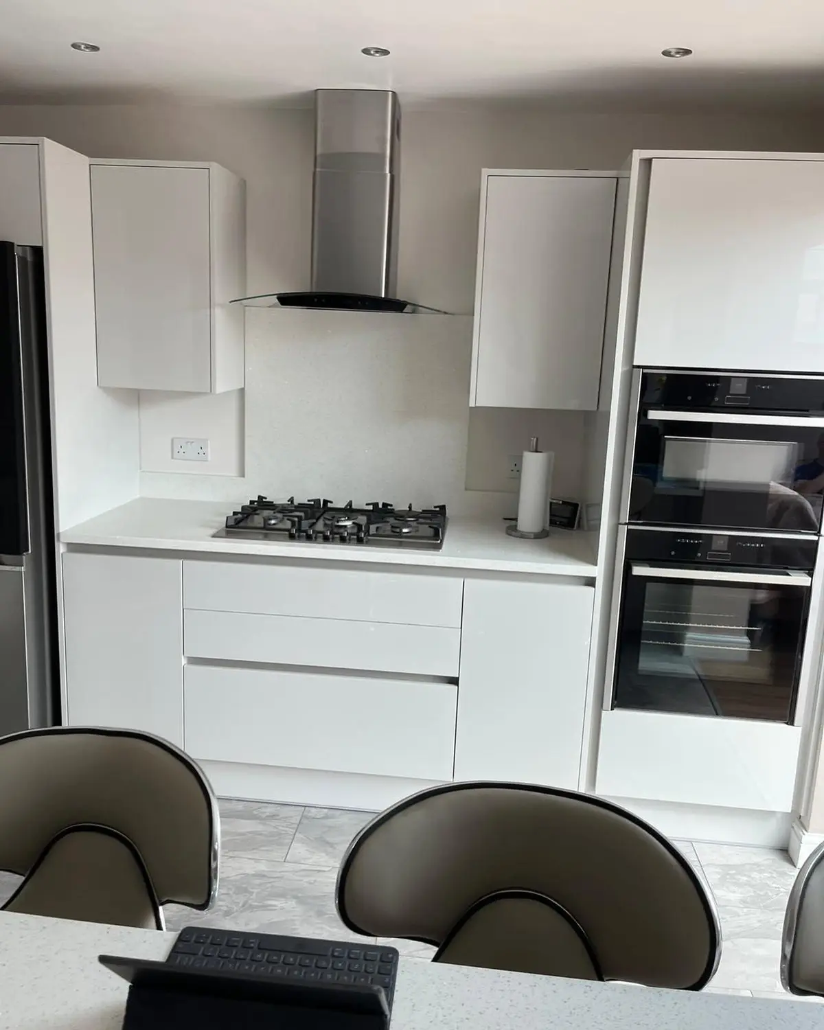 Light handleless kitchen with white worktop, gas hob, chimney extractor and built-in double oven