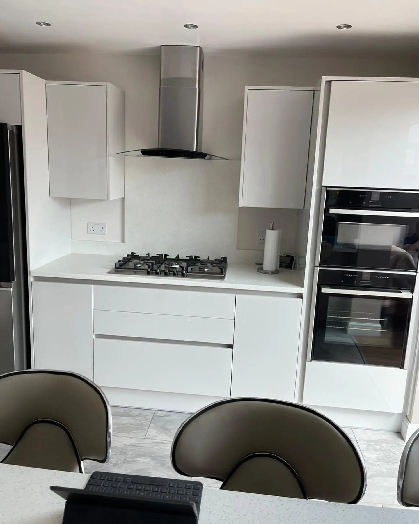 Light handleless kitchen with white worktop, gas hob, chimney extractor and built-in double oven