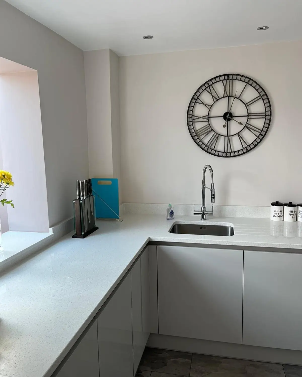 Pale grey handleless corner run with white quartz worktop and a large wall clock