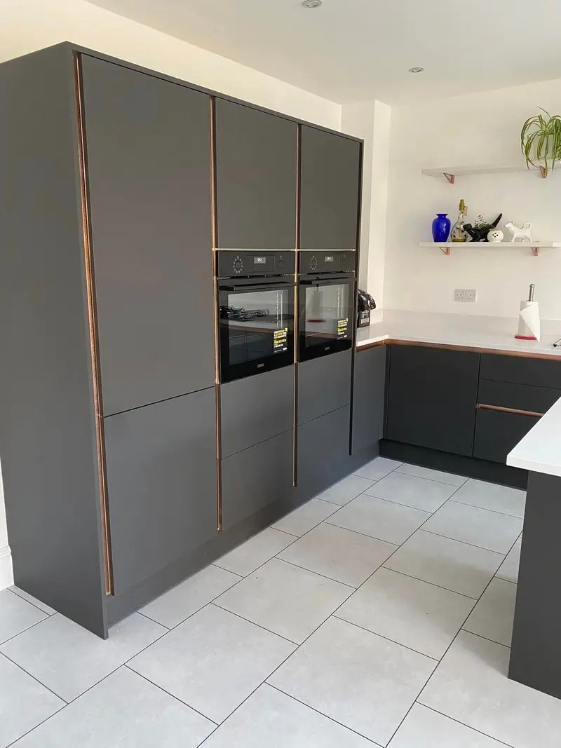 Bank of tall dark grey handleless units with two built-in ovens and copper vertical profiles