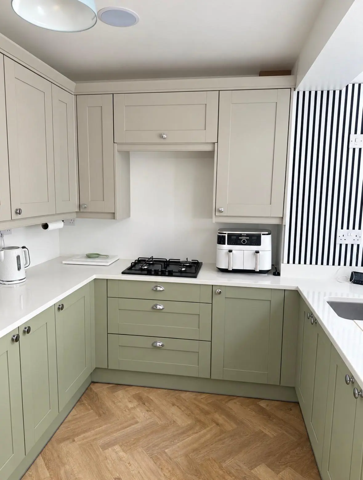 Green sage base units and cashmere wall units around a gas hob, with white quartz worktops