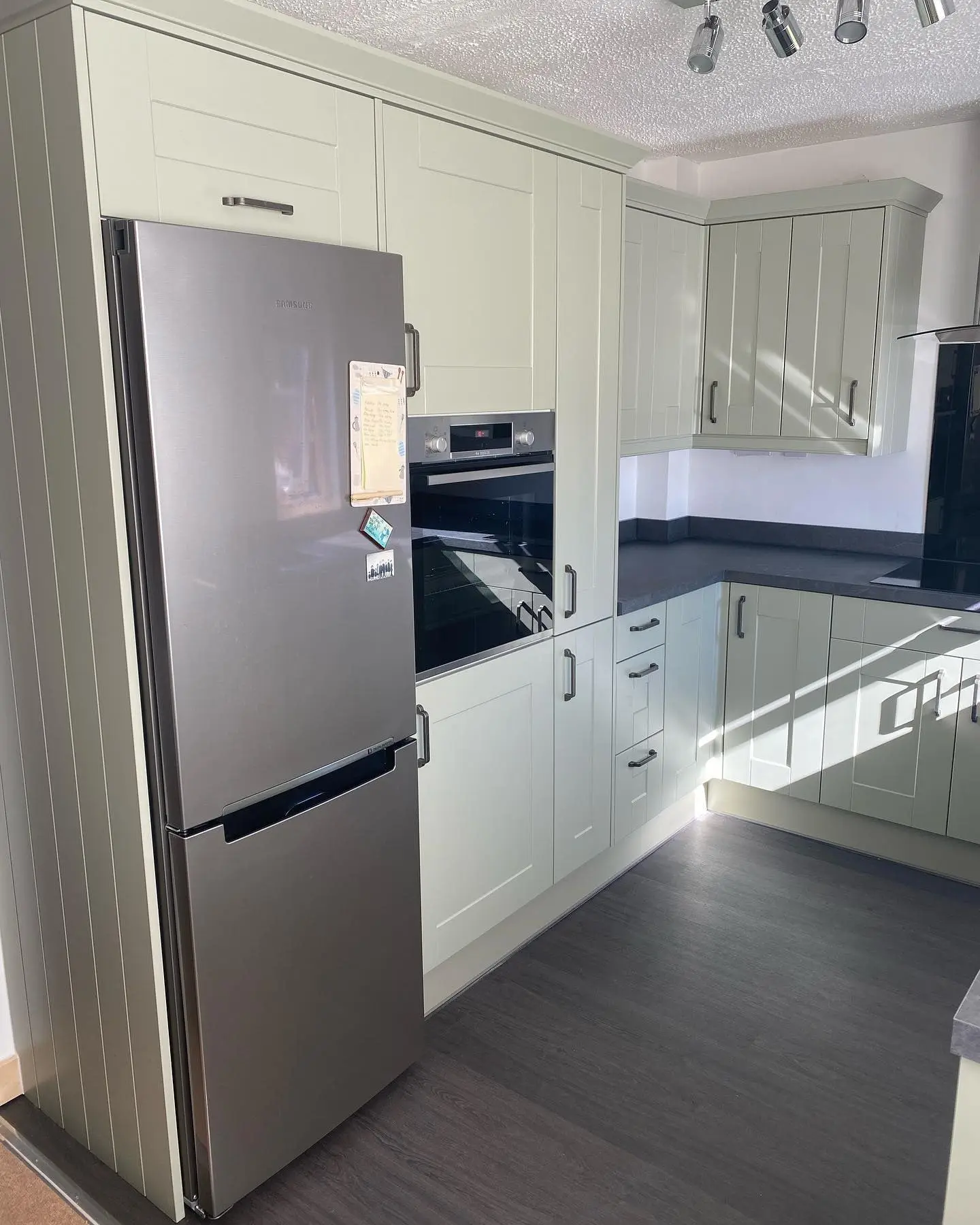 Pale sage shaker kitchen with grey worktops and upstands, black glass splashback and chimney extractor