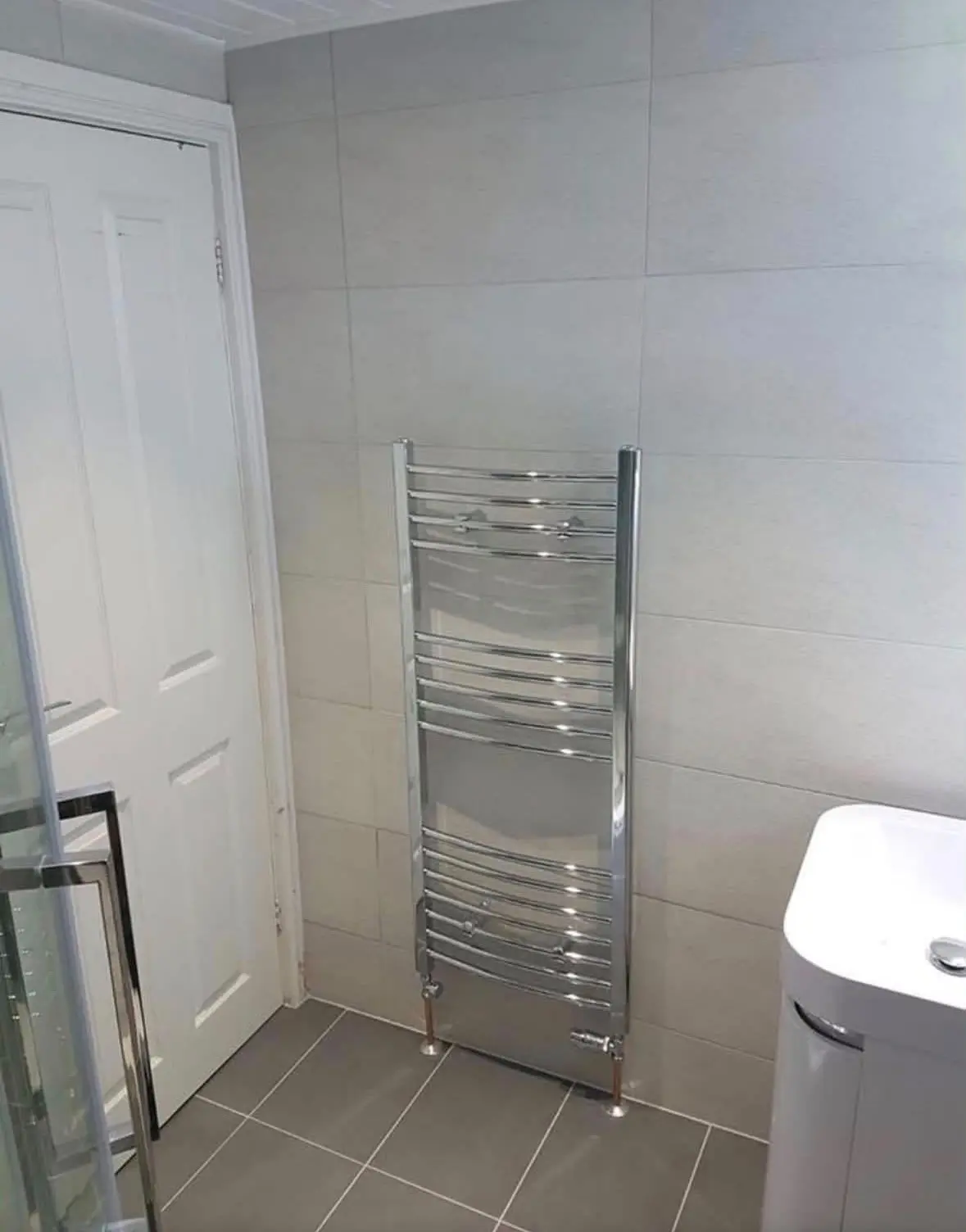 Chrome towel radiator beside the door, with grey floor tiles