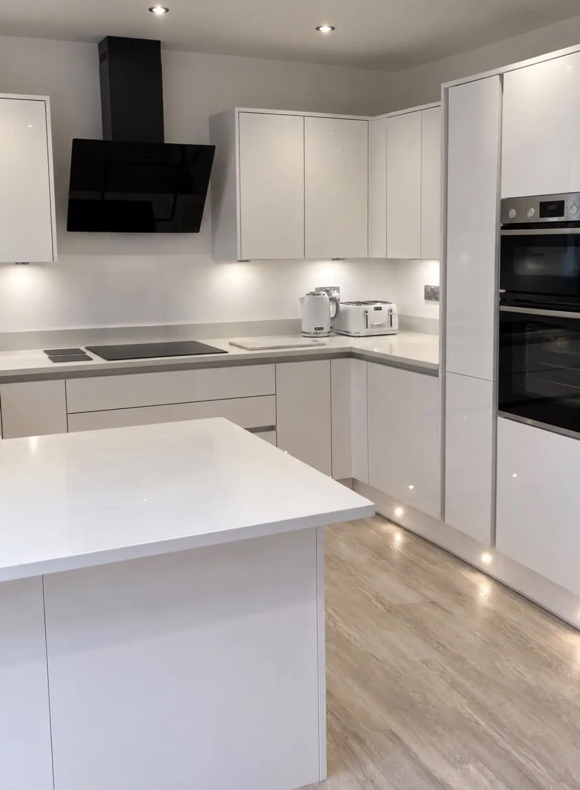 White gloss handleless kitchen with an angled black extractor, island and plinth lights