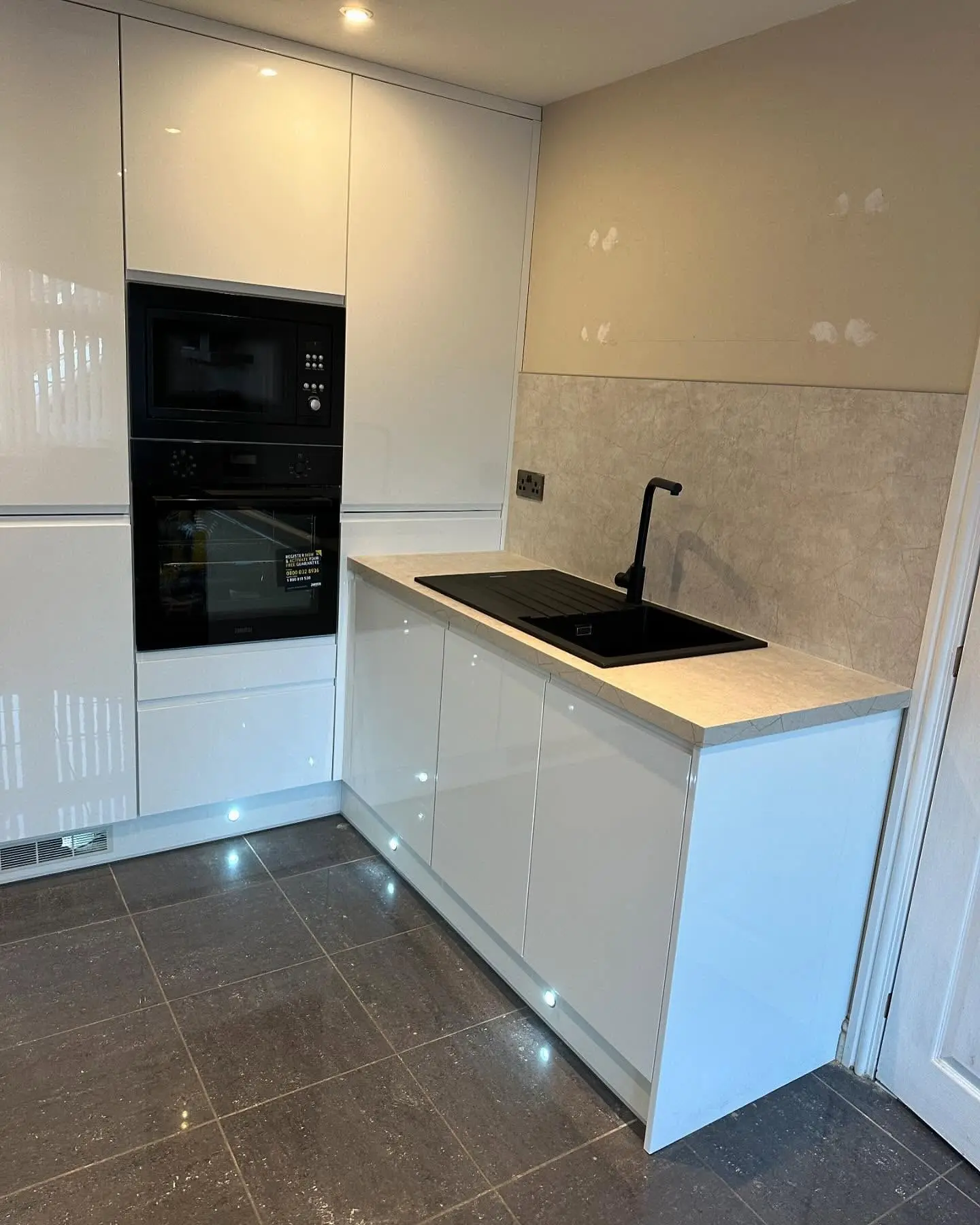 White high-gloss handleless kitchen with black built-in ovens and plinth lights