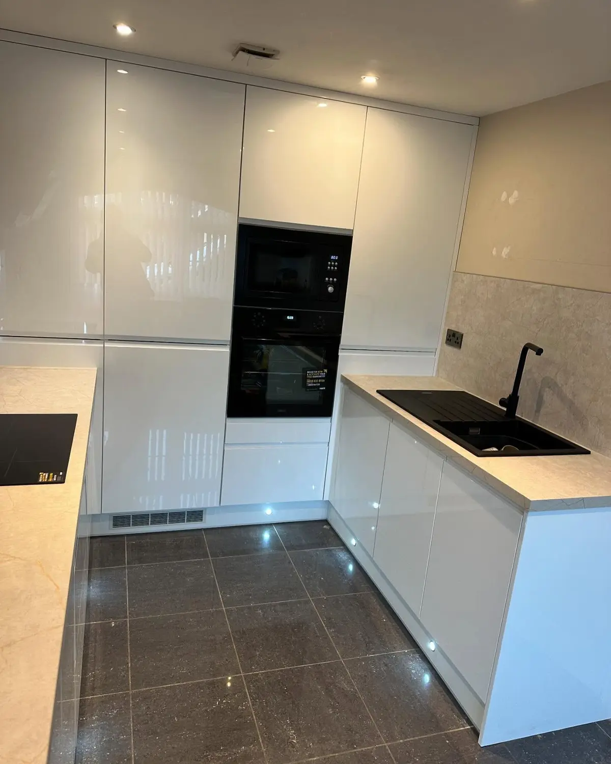 White gloss kitchen with black built-in ovens and a stone-effect splashback