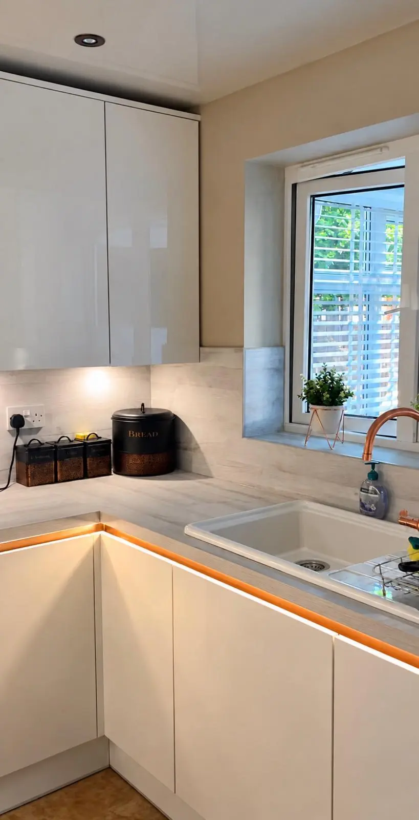 Sink run beneath the window, with warm white strip lights along the gold Milano rails