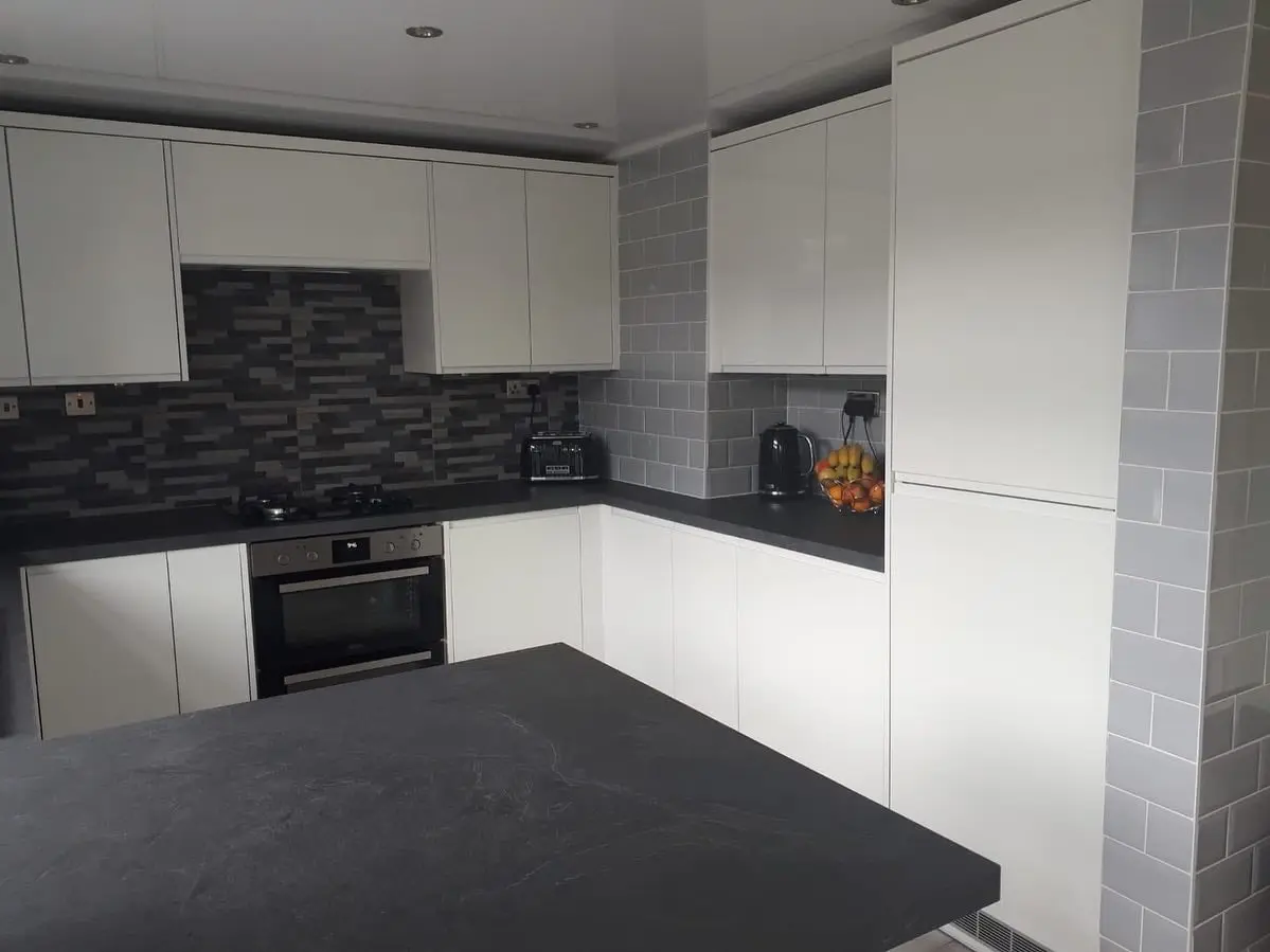 Finished white handleless kitchen with black worktops and a mosaic splashback