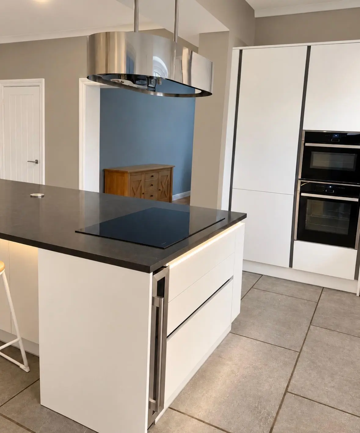 White handleless island with black quartz worktop, hob and strip lighting