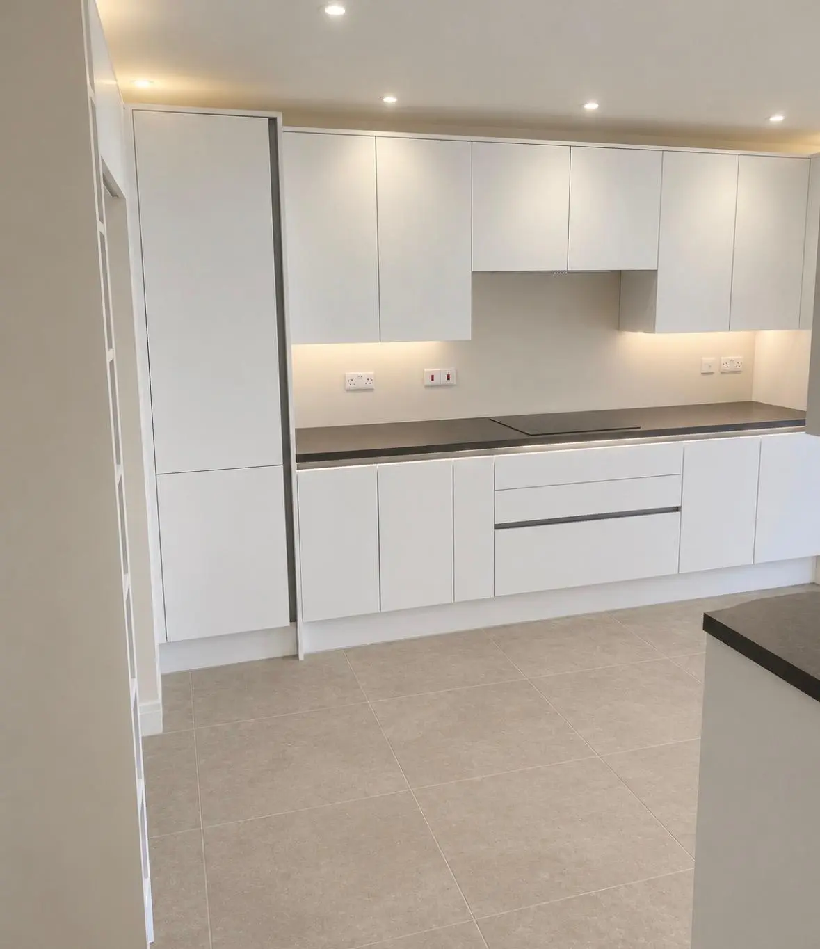 White handleless run with a tall unit, black worktop and under-cabinet lighting